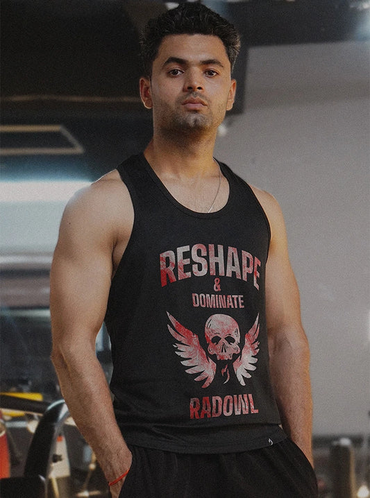 Front view of a muscular male model wearing the Hellbound Black Stringer in a gym setting, showcasing the bold skull and wings design with Radowl's slogan 'Reshape and Dominate,' capturing strength and fitness focus.