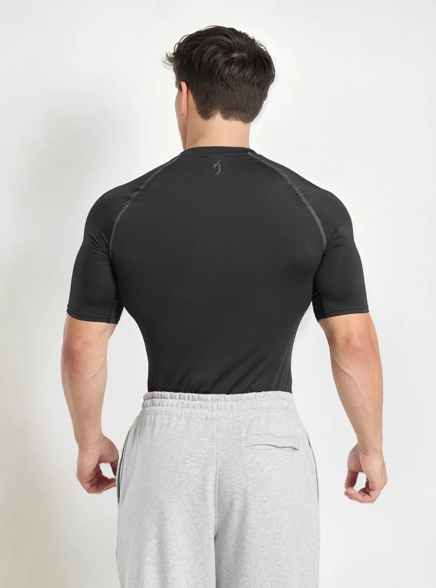 Back view of gym model wearing dark domination half sleeve compression tshirt standing on whitebackdrop background.